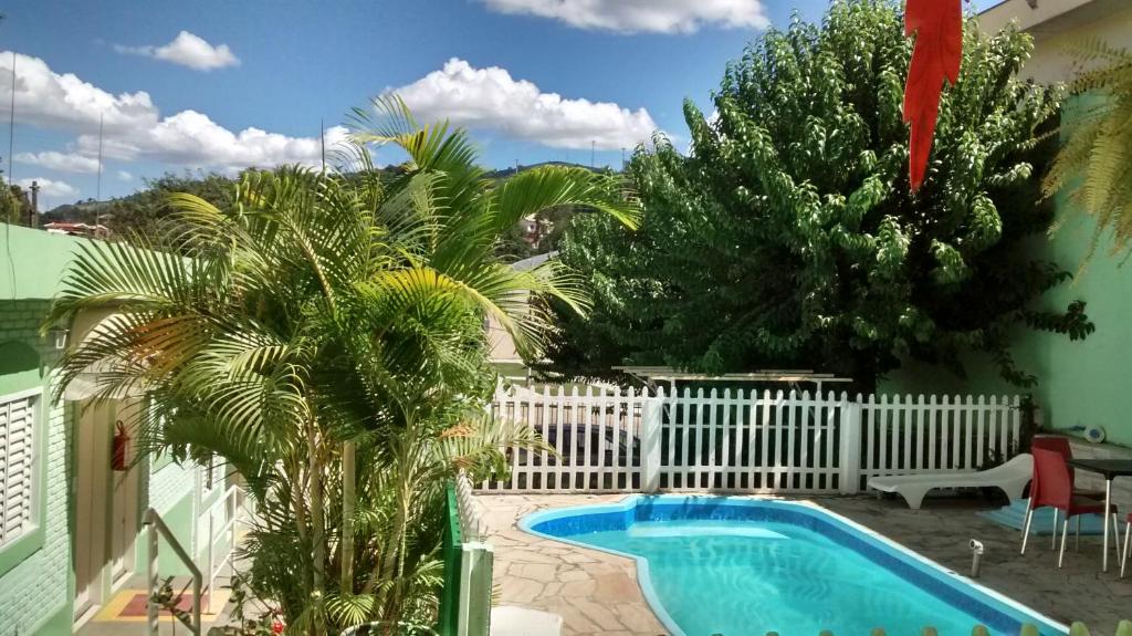 a pool in a yard with a white fence and palm trees at Pousada Encanto Das Aguas in Lindóia