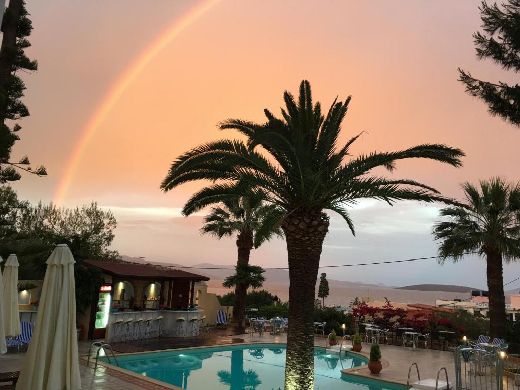 a rainbow over a pool with a palm tree at Tolon Holidays Hotel in Tolo