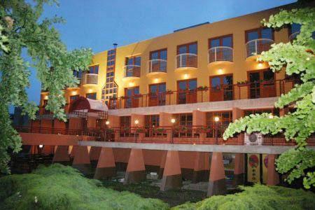 un grand bâtiment avec des tables et des chaises devant lui dans l'établissement Hotel Minerva, à Mosonmagyaróvár