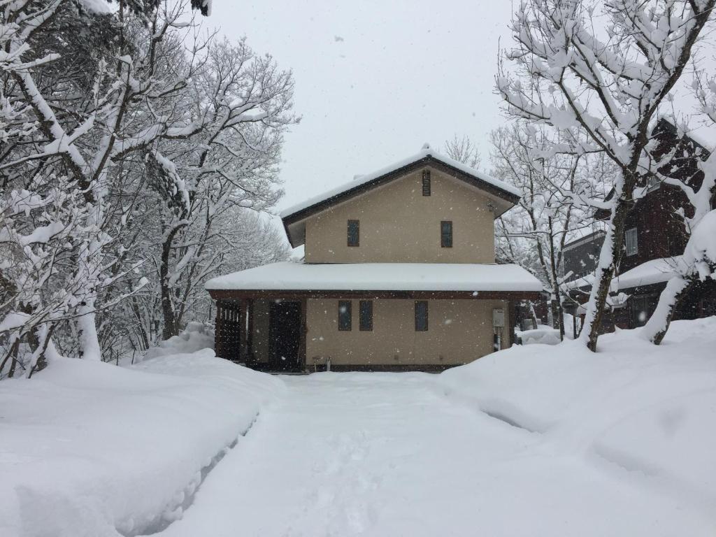 a house covered in snow in a snowy yard at Shirokuma Lodge Hakuba in Hakuba