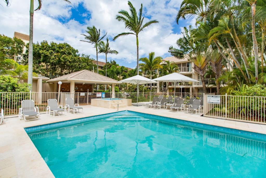 a swimming pool with chairs and palm trees at Miami Beachside Holiday Apartments in Gold Coast