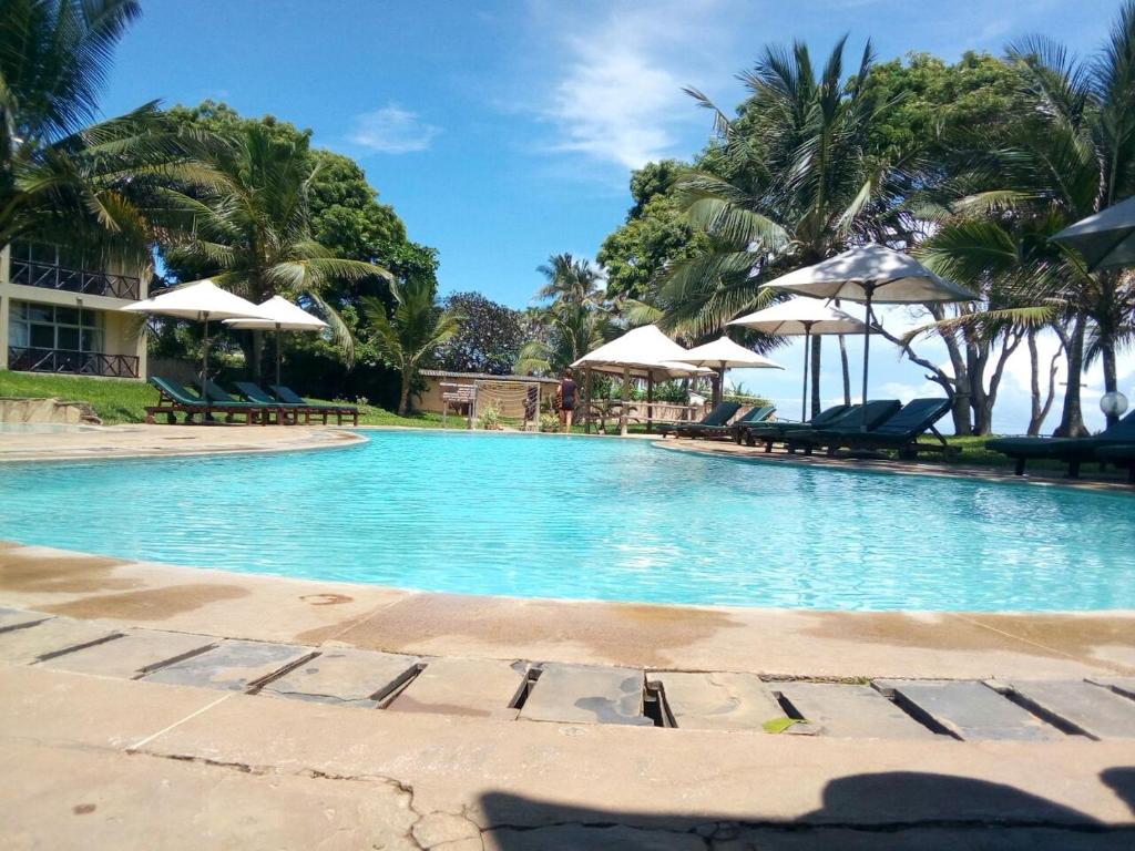 a swimming pool with palm trees and umbrellas at Coral Beach Resort in Diani Beach