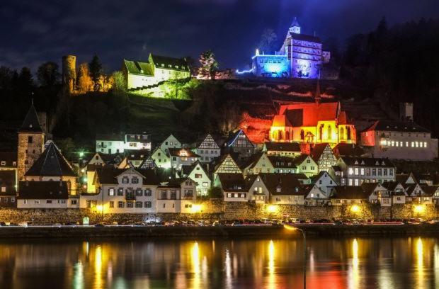 a city lit up at night next to the water at Natur und Neckarblick bei Heidelberg in Hirschhorn
