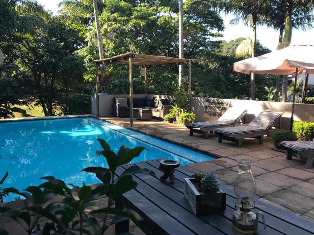 a swimming pool with a table and benches and an umbrella at Beach Forest Lodge in Ballito