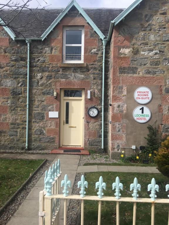 a brick house with a white door and a fence at 1 Lochness Rooms&Hostel in Drumnadrochit