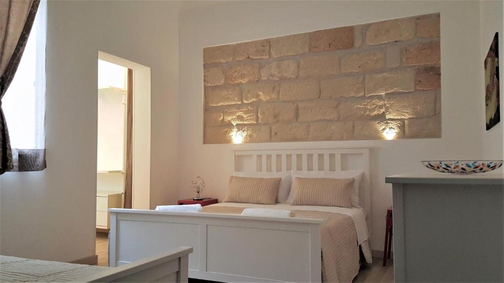 a bedroom with a white bed and a stone wall at NoMapartments Il Cortile Romey in Trapani