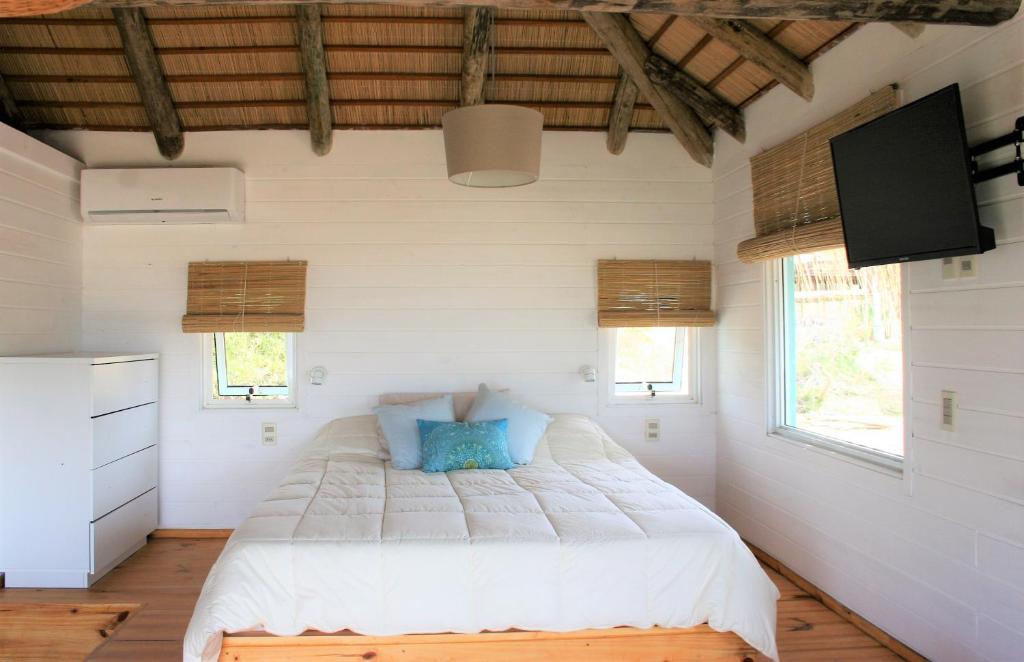 1 dormitorio con 1 cama blanca grande con almohadas azules en Cabaña PRAIA, en Punta del Diablo