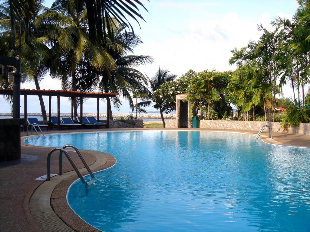 a large blue swimming pool with palm trees and the ocean at Bann Pae Cabana Hotel And Resort in Klaeng