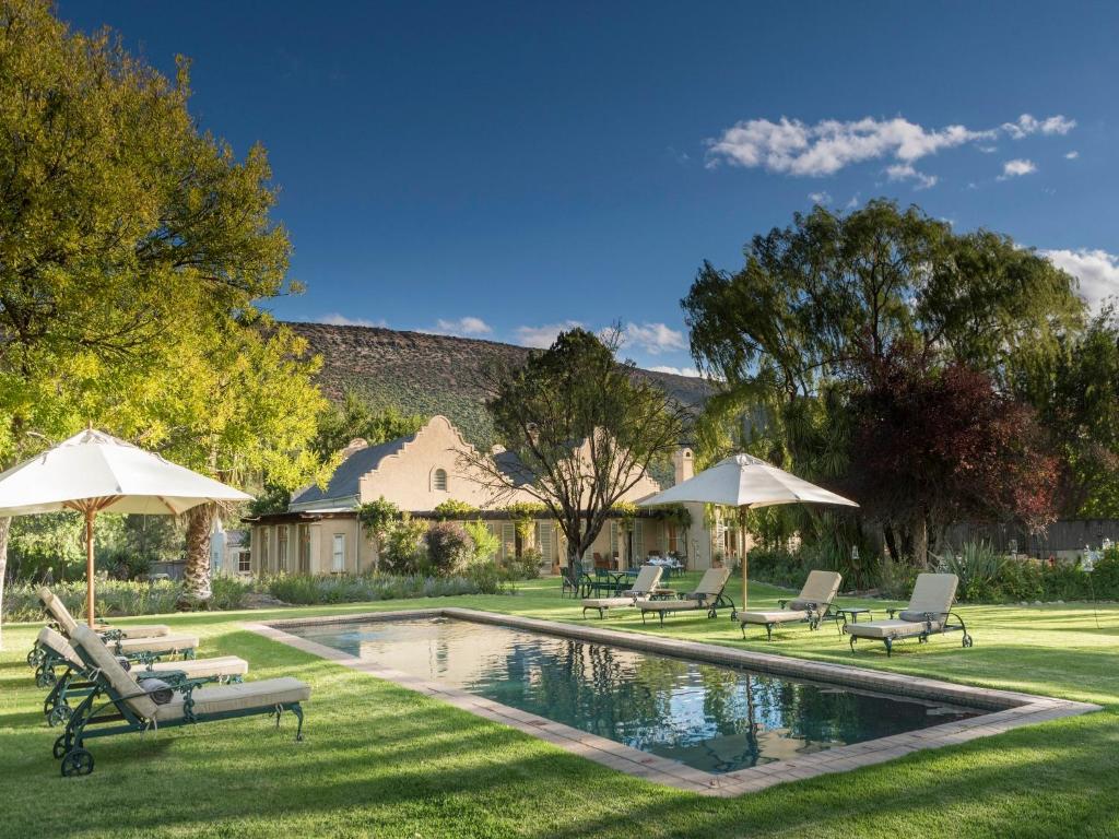 a pool with chairs and umbrellas in a yard at Mount Camdeboo Private Game Reserve by NEWMARK in Graaff-Reinet