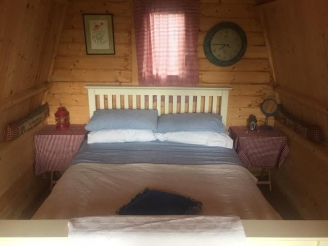 1 cama en una cabaña de madera con reloj en la pared en Littlebridge Farmhouse en Bude