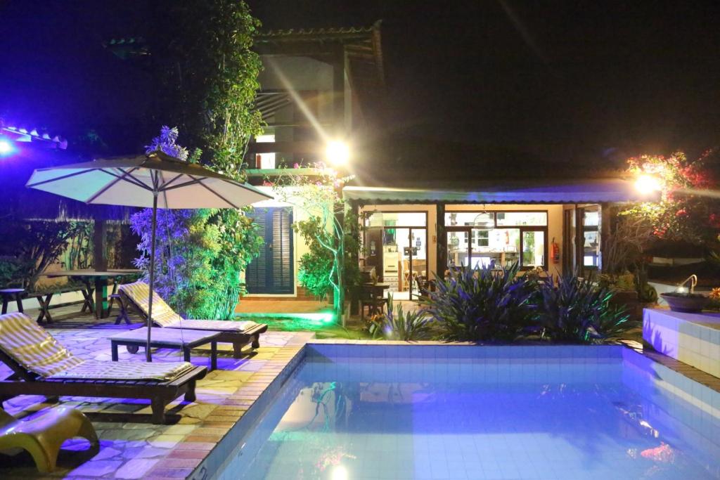 a swimming pool at night with a table and an umbrella at Pousada Solar Dos Corais in Búzios