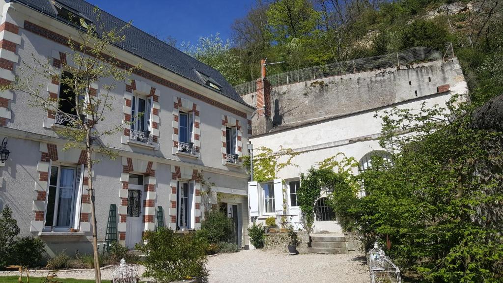 un antiguo edificio blanco junto a una montaña en Les Troglos de la Tufolière, en Rochecorbon