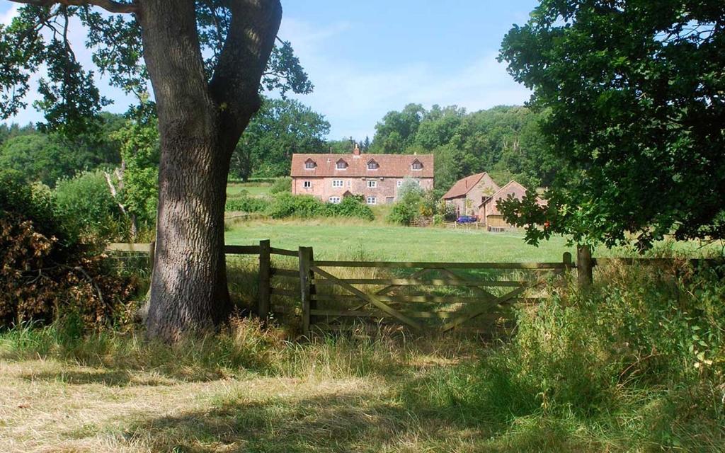 una valla y un árbol en un campo con una casa en Grove Farm B&B en Newnham