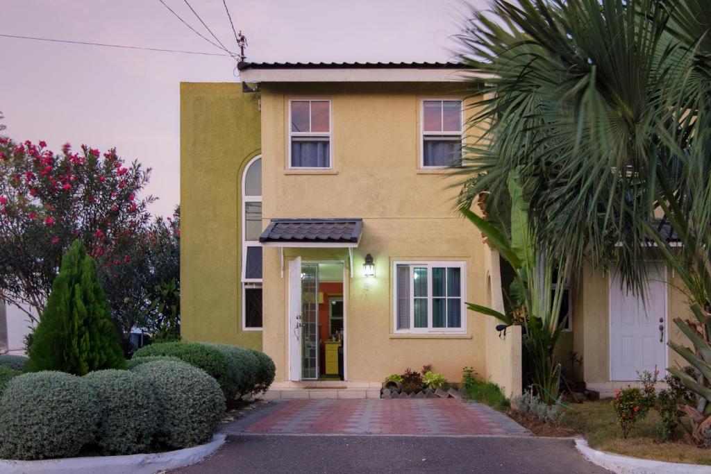 a yellow house with a white door and some bushes at Country Club Comfort in Portmore