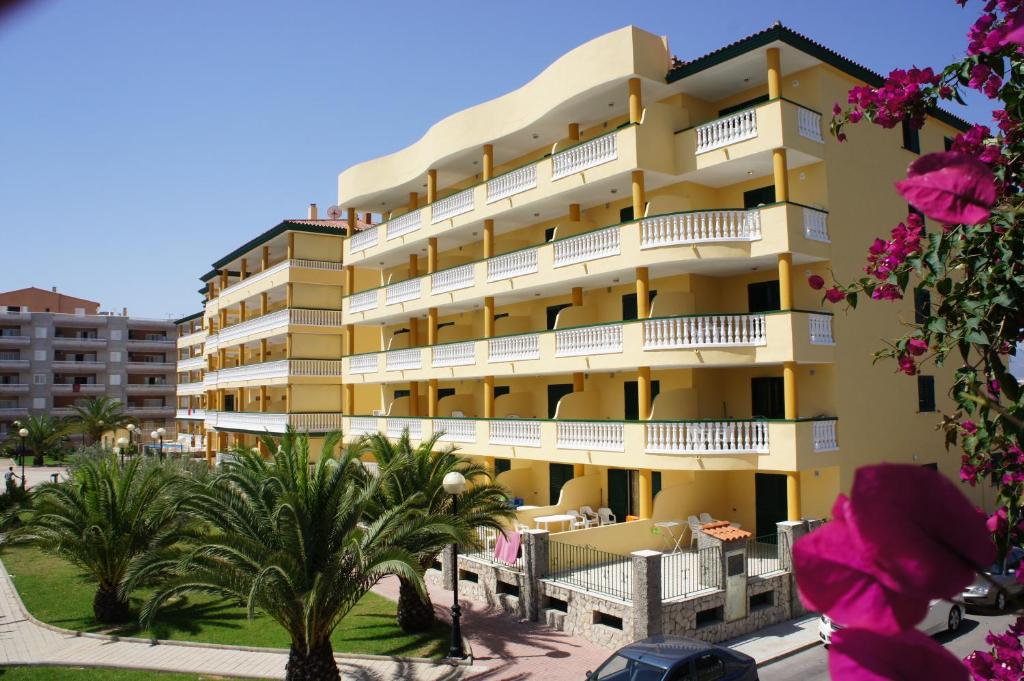 un edificio de apartamentos amarillo con palmeras y flores rosas en Apartamentos Satse Moncofa, en Moncófar