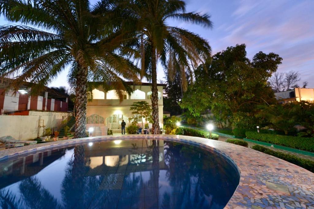 a swimming pool with two palm trees in front of a house at One World Village Guesthouse in Bakau