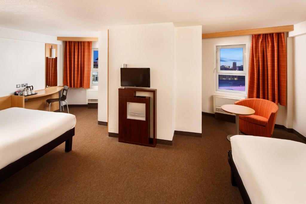 a hotel room with two beds and a desk and a television at ibis Birmingham Centre New Street Station Hotel in Birmingham
