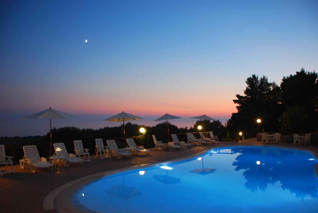 uma piscina com cadeiras e guarda-sóis ao anoitecer em Resort Paradise Marina di Camerota em Marina di Camerota