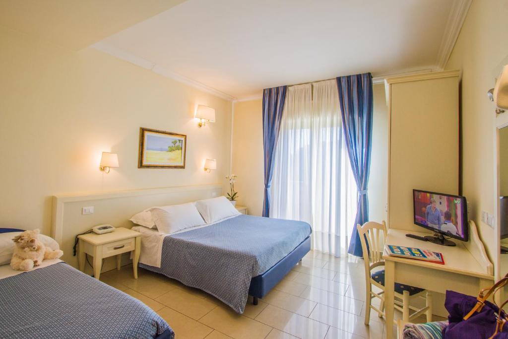 a bedroom with two beds and a desk and a window at Hotel Nelson in Riccione