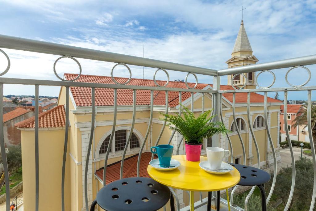 un balcón con una mesa y sillas amarillas y una iglesia en Apartments in city center Ventus, en Novalja