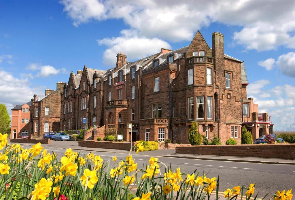 a large brick building with yellow flowers in front of it at Cairndale Hotel in Dumfries