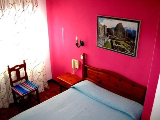 Dormitorio rosa con cama y silla en Hostal Cuzco, en Salamanca