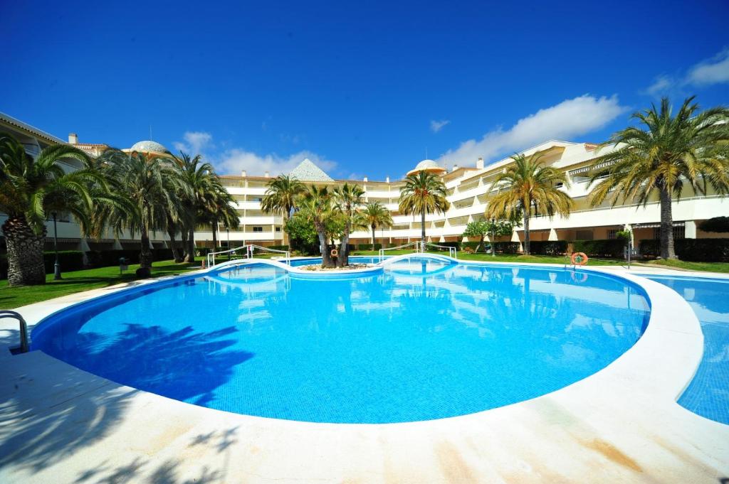 une grande piscine avec des palmiers en face d'un bâtiment dans l'établissement Las Terrazas - Orange Costa, à Alcossebre