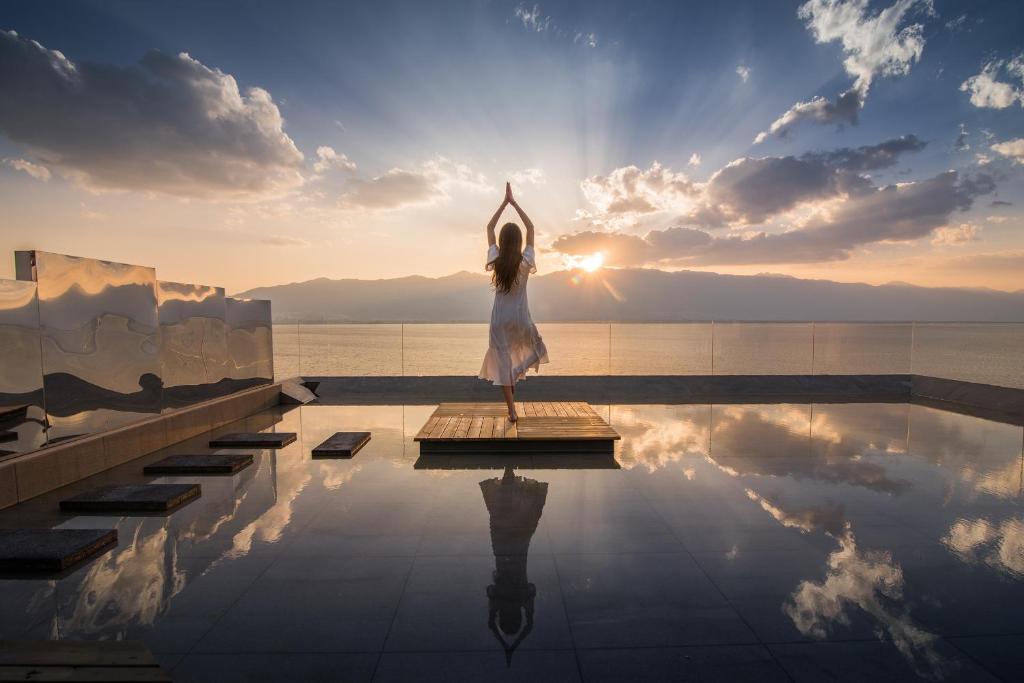 una mujer vestida de blanco haciendo yoga junto a la piscina en Yuanshanqing·Stone Hill Seaview Guesthouse, en Dali