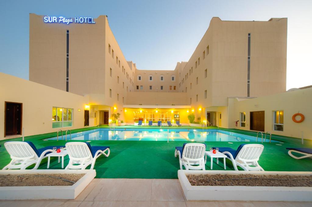 a pool at a hotel with white chairs and a building at Sur Plaza Hotel in Sur