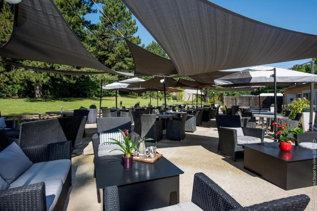 an outdoor patio with tables and chairs and umbrellas at Logis Hôtel La Magnanerie - Côté Bistro in Aubignosc