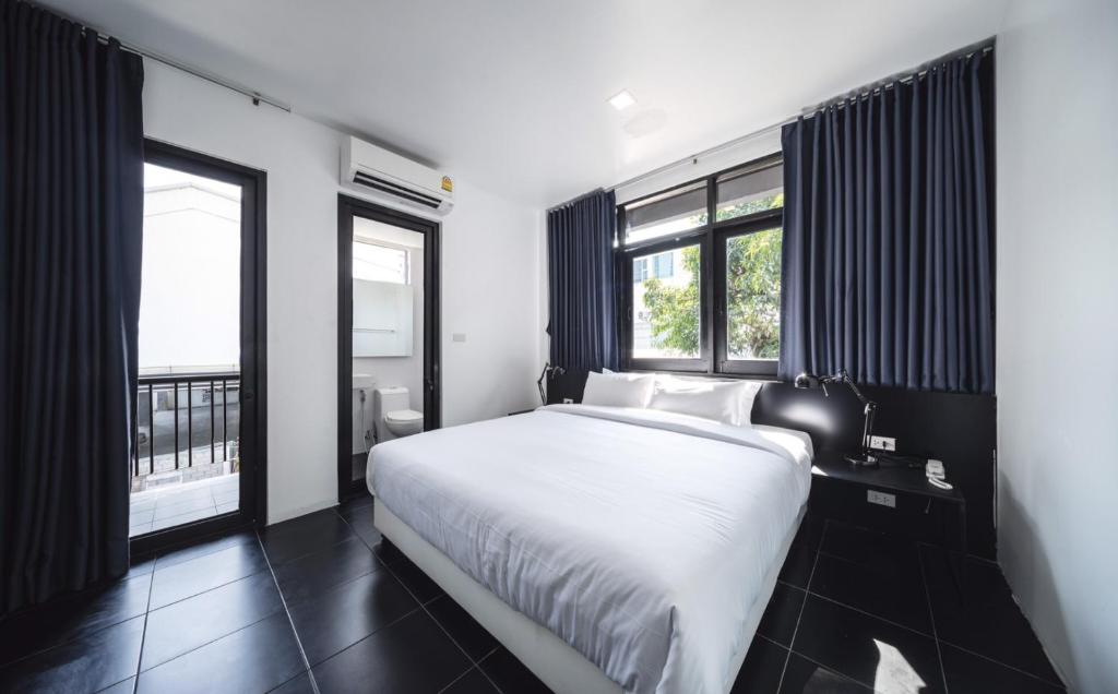 um quarto com uma cama branca e 2 janelas em The Common Hostel em Chiang Mai