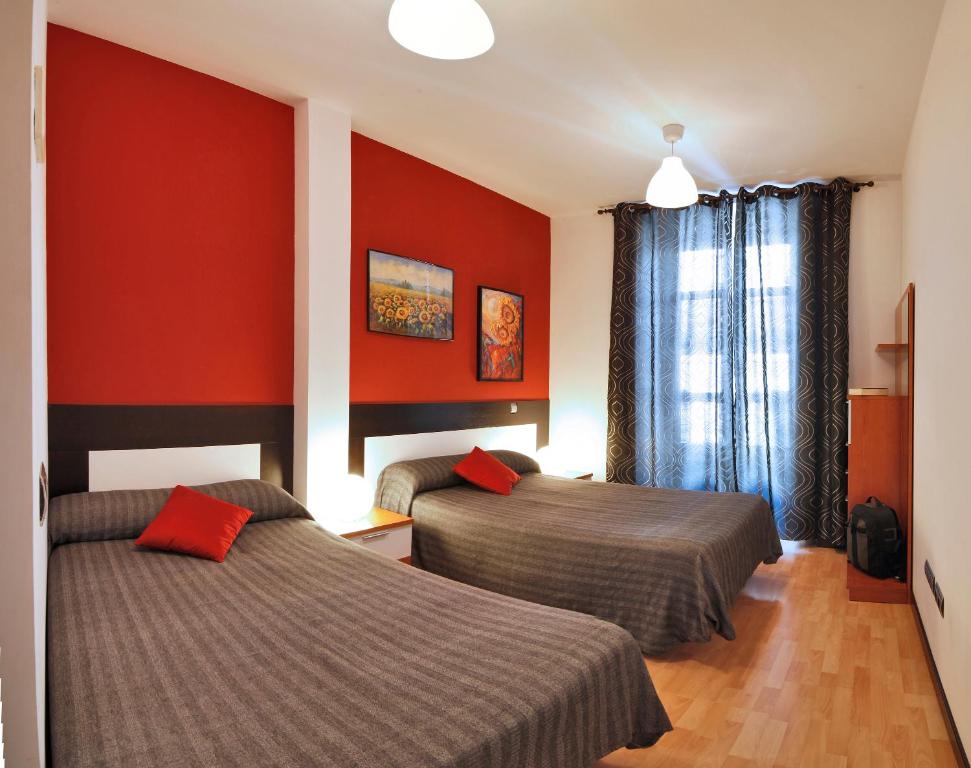 2 camas en una habitación de hotel con paredes rojas en Apartamentos El Tiempo Madrid, en Madrid