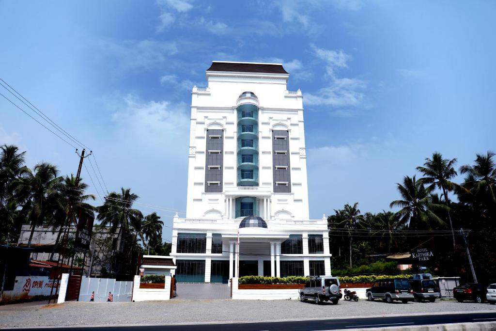 un alto edificio bianco con macchine parcheggiate di fronte di Hotel Karthika Park a Kazhakuttam