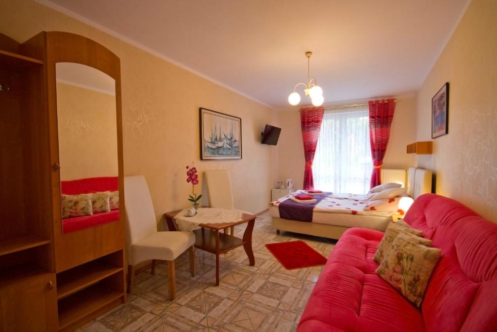 a living room with a red couch and a bedroom at Victoria Dom Wczasowy in Krynica Morska