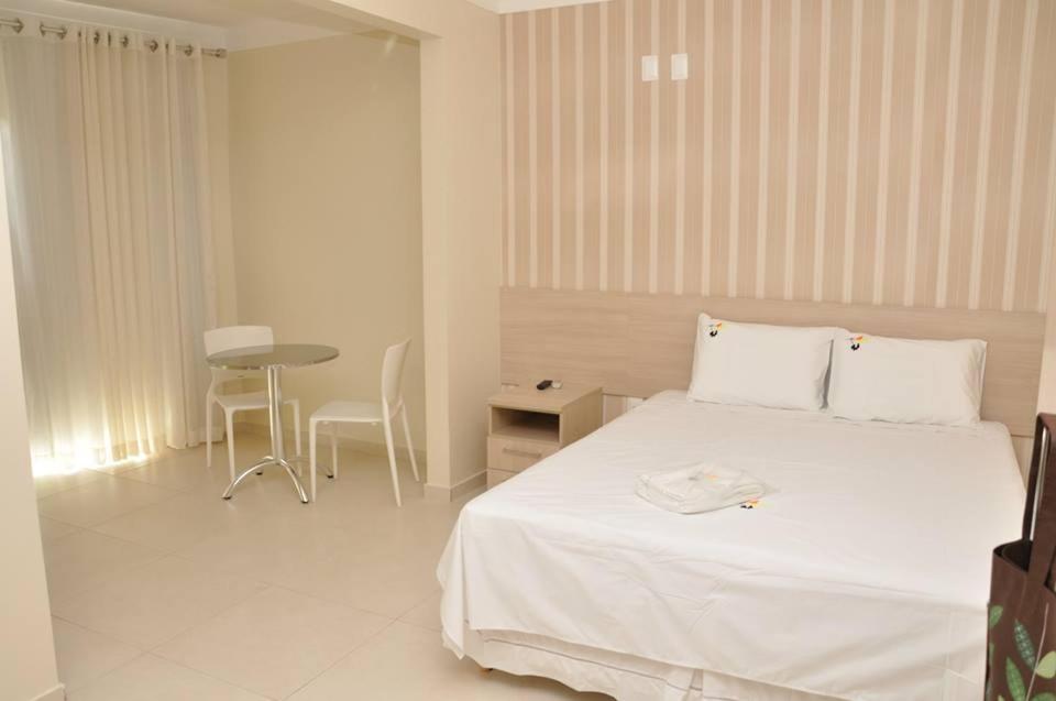 a white bedroom with a bed and a table at Beija - Flor Hotel in Ipiaú
