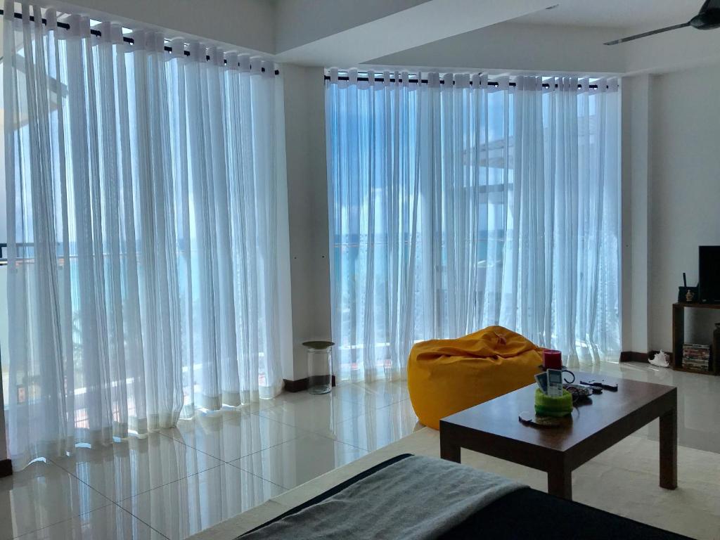 a living room with white curtains and a table and a couch at Araliya OceanFront Condos Nilaveli, Trincomalee in Nilaveli