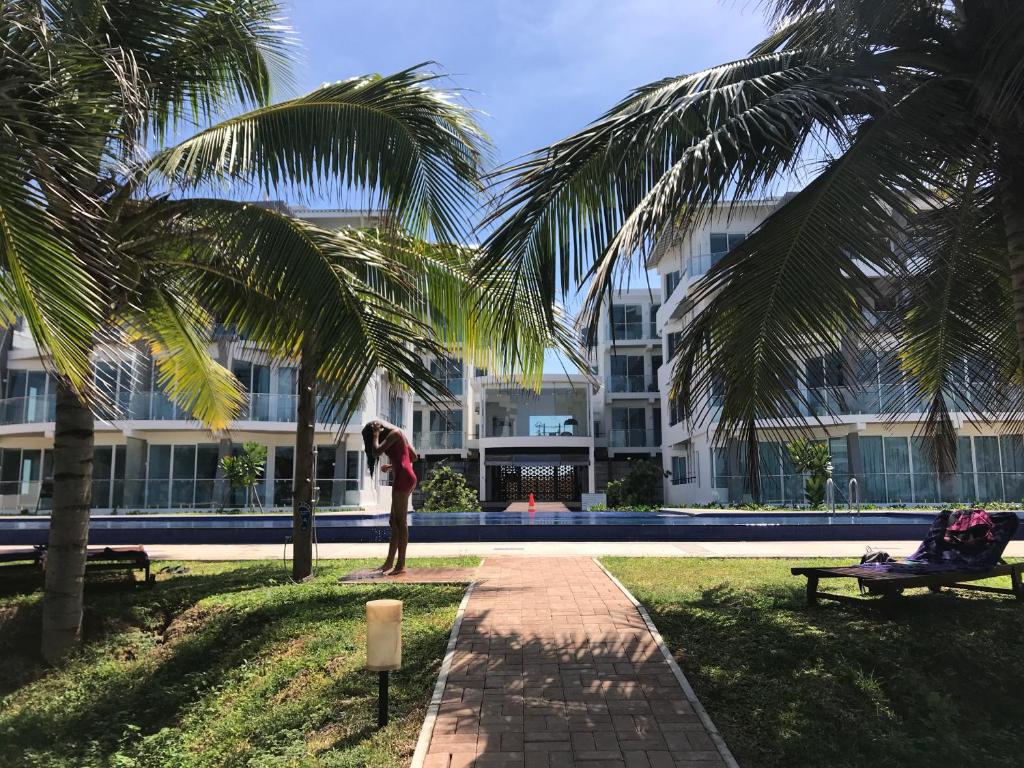 a woman standing under a palm tree in front of a building at Araliya OceanFront Condos Nilaveli, Trincomalee in Nilaveli