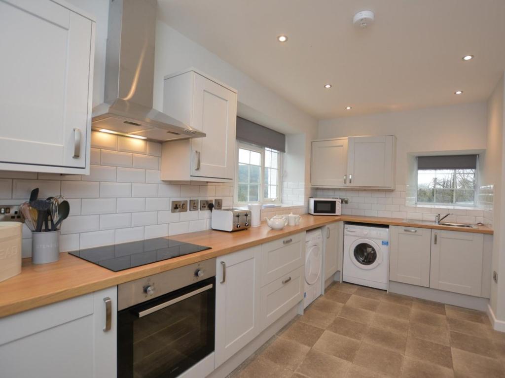 a kitchen with white cabinets and a washer and dryer at Pengarreg Fawr in Llanilar