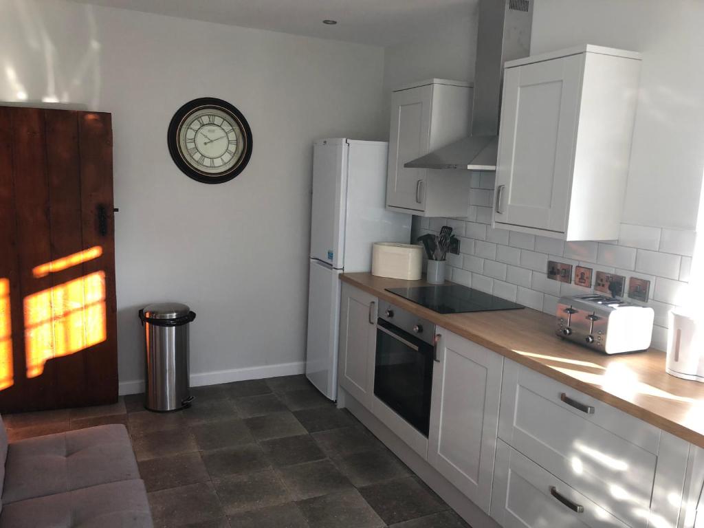 a kitchen with white cabinets and a clock on the wall at Pengarreg Fawr in Llanilar