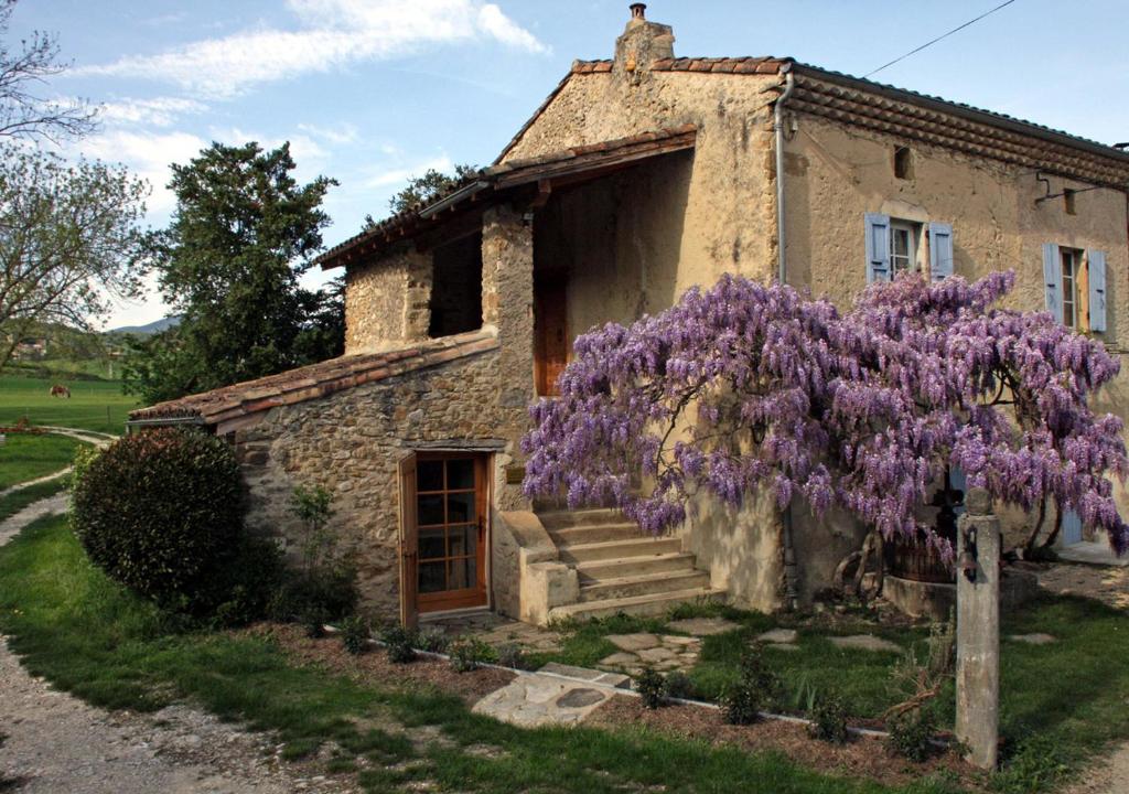 uma velha casa de pedra com uma coroa de flores roxas em Touroulet em Suze