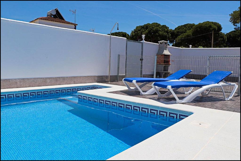 a swimming pool with two blue chairs next to a fence at Casa Rural Zara II in Conil de la Frontera