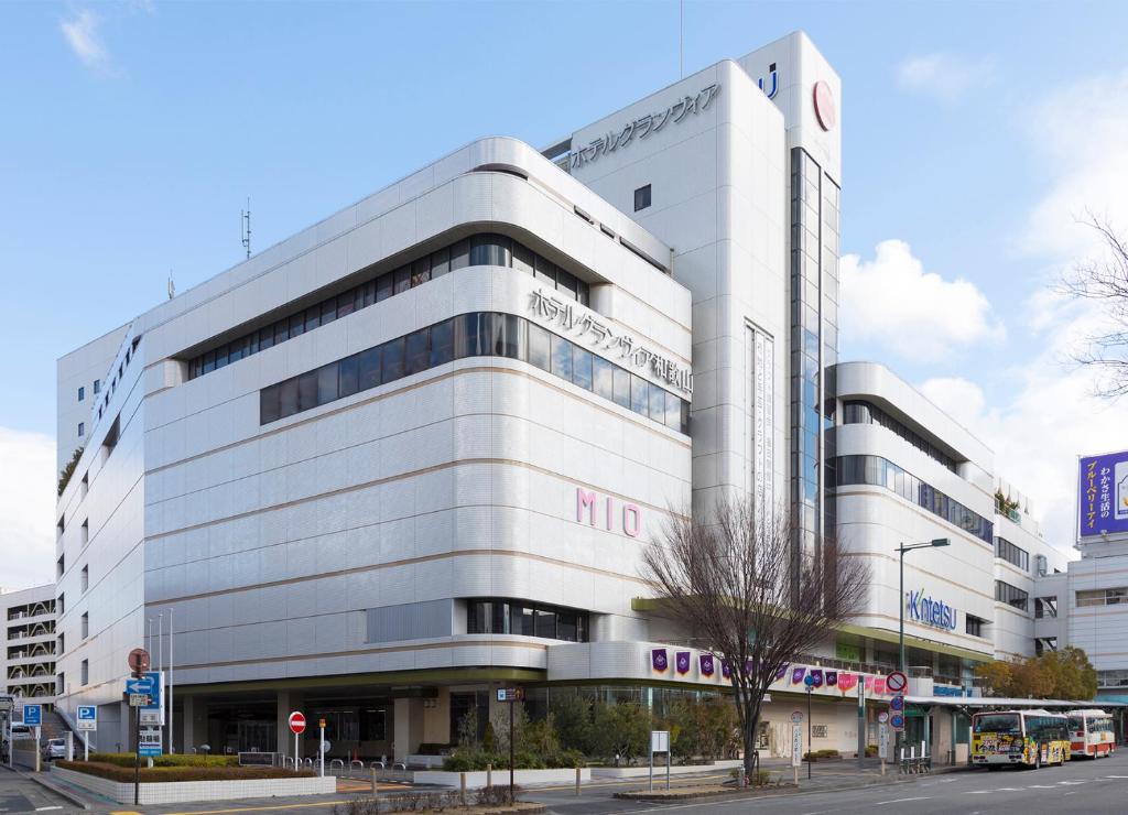 um grande edifício branco com um autocarro estacionado em frente em THE S3 Wakayama Station em Wakayama