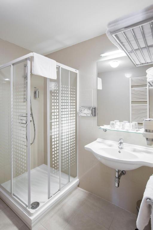 a white bathroom with a shower and a sink at Hotel Páv in Prague