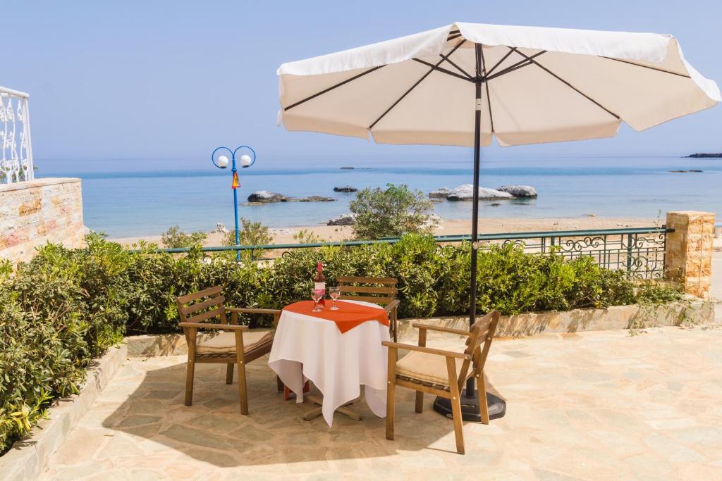 a table with an umbrella and chairs and the beach at Kaya Sea Apts - Stegna Beach in Archangelos
