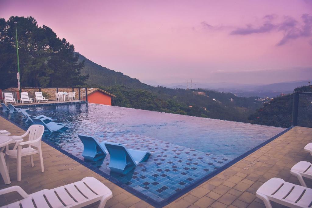 uma piscina com cadeiras brancas e uma montanha em Hotel Refúgio Vista Serrana em Mairiporã