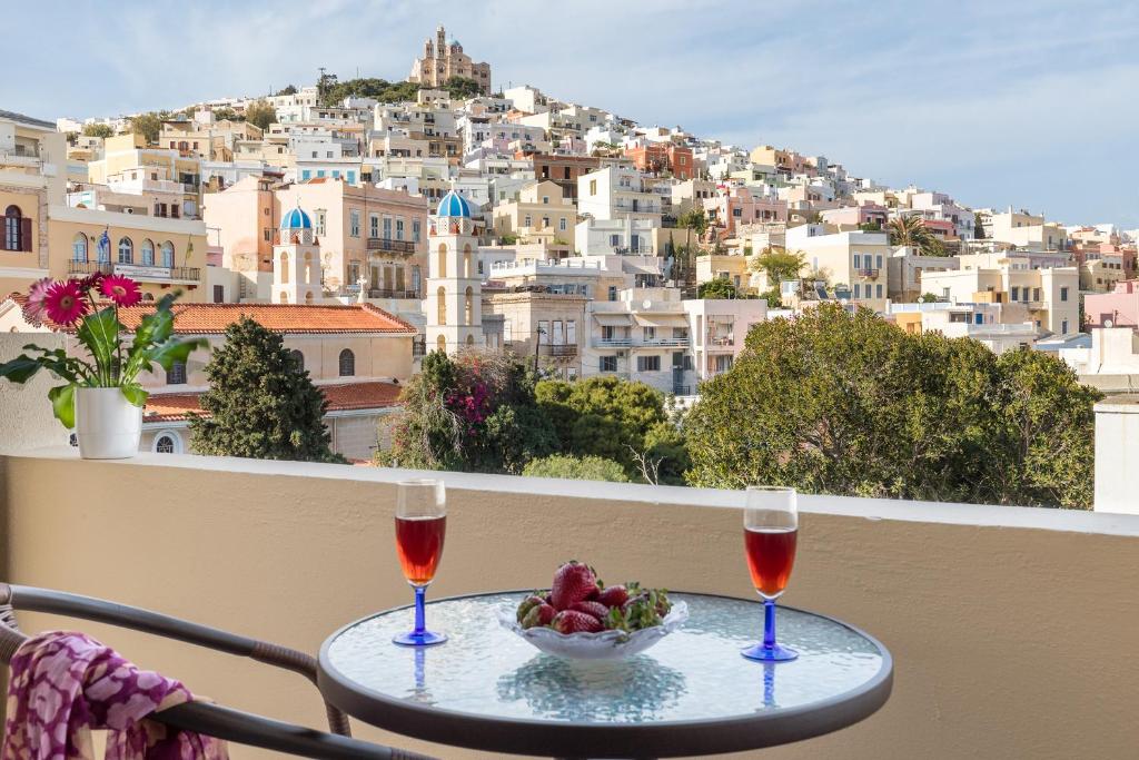 a table with two wine glasses and a bowl of fruit on a balcony at Iliada in Ermoupoli