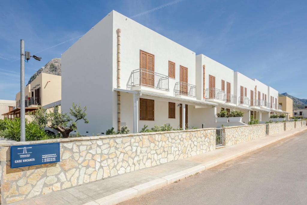 a white building with a stone wall next to a street at Case Vacanza appartamenti Trinacria in San Vito lo Capo