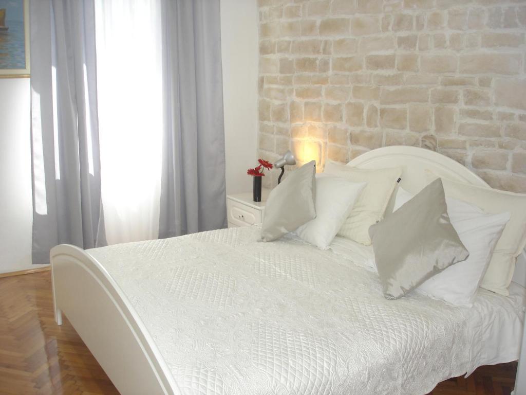 - un lit blanc avec des oreillers blancs et un mur en briques dans l'établissement Apartment Lilly, à Split