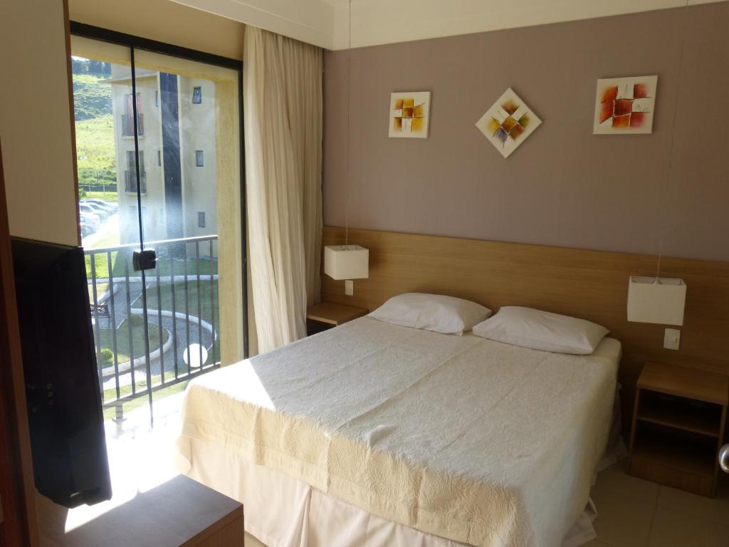 a bedroom with a white bed and a balcony at Aldeia das Águas Park Resort - Flat Quartier in Barra do Piraí