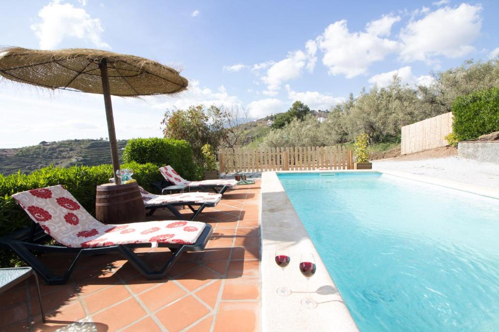 a swimming pool with two chairs and an umbrella at Holiday House ¨Montepiscina¨ in Cómpeta